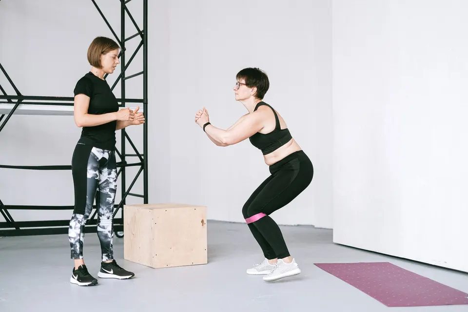 Een trainster kijkt mee terwijl een klant een squat doet met een elastiek